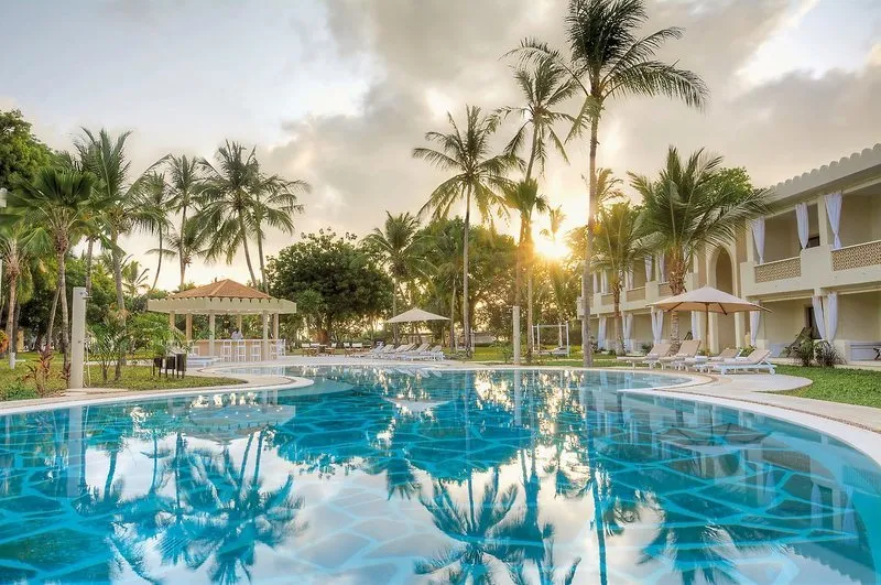 Moderen hotelski bazen ob sončnem zahodu z odsevi palm